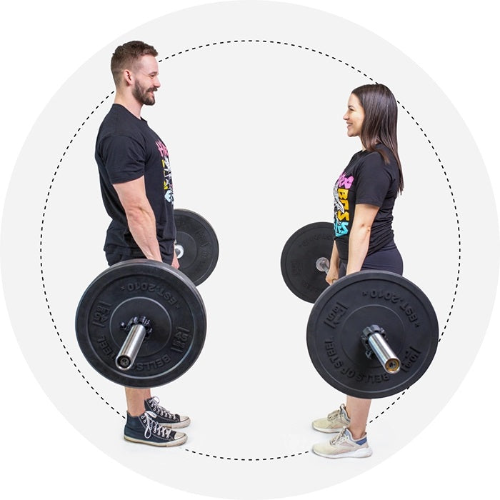 In a white background with a dotted circle, a man and woman hold Partner Bar Bumper Sets at their sides. Both are clad in black workout gear and sneakers.