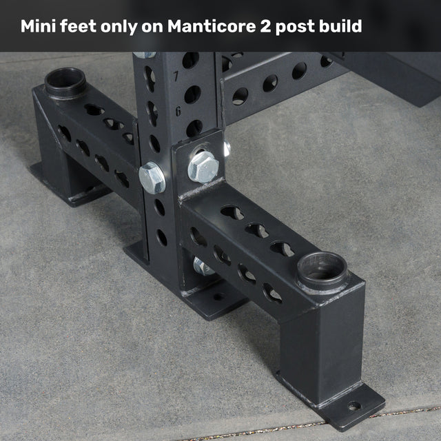Close-up of the mini feet attachment on a Bells of Steel Manticore Two Post Converter Bench, featuring black metal supports with multiple bolt holes and large bolts securing the bench to a concrete floor.