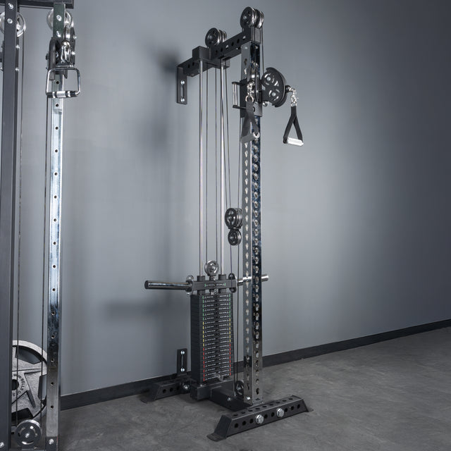 The Bells of Steel Oblivyon Tower - 3" x 3” Cable Tower stands against a gray wall in a gym, featuring adjustable weights, pulleys, and a single handle attachment on the right, set on a smooth concrete floor.