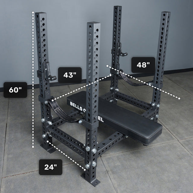 A black Manticore Four Post Converter Bench by Bells of Steel sits on a gray floor, measuring 60" tall, 48" wide, 24" deep, with 43" between uprights. "BELLS" is printed on its side.
