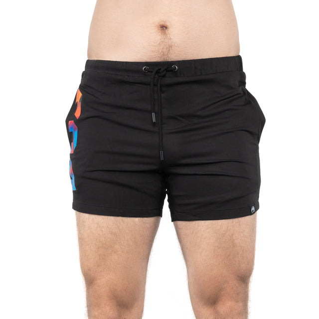 A person in mid-thigh-length Bells of Steel Gym Shorts stands against a white background. The black high-performance shorts feature a drawstring and a colorful design on the left side.