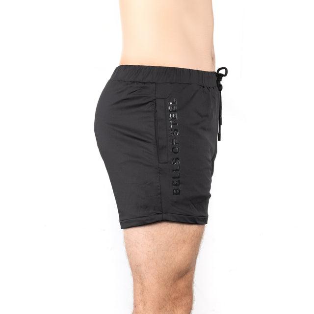A person is shown from waist to mid-thigh in side profile wearing Bells of Steel Gym Shorts, featuring "BELLS OF STEEL" written vertically on the left side, set against a white background.