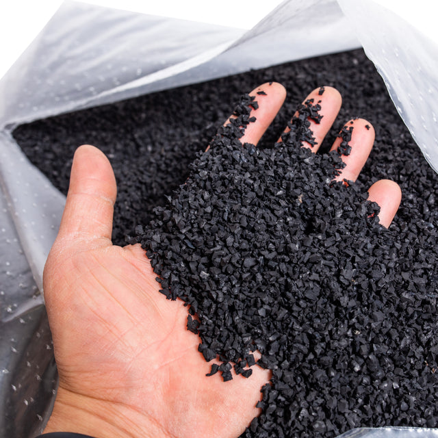 A hand scoops up Bells of Steel Recycled Tire Rubber Crumb Filler from a 40lb bag—eco-friendly material made from recycled tires.