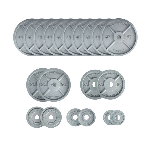 The Bells of Steel Machined Iron Olympic Weight Plate Sets feature gray plates in 45, 35, 25, 10, 5, and 2.5 lb sizes arranged in rows. Each has a precision hole for reliable weight tolerance.