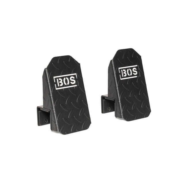 Two black, rectangular metal Footplates for Cable Tower/All In One Trainer by Bells of Steel feature angled faces, a diamond plate texture, and the white "BOS" logo—perfect accessories set against a clean white background.
