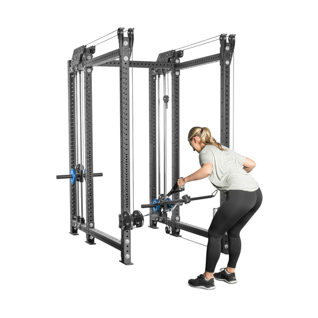 A person uses the Kraken Rack Attachment for 6 Post Manticore Racks (Single Side) by Bells of Steel to perform a bent-over row. Wearing a gray shirt and black pants, they grip the handle in a gym setup featuring adjustable weights and pulleys.