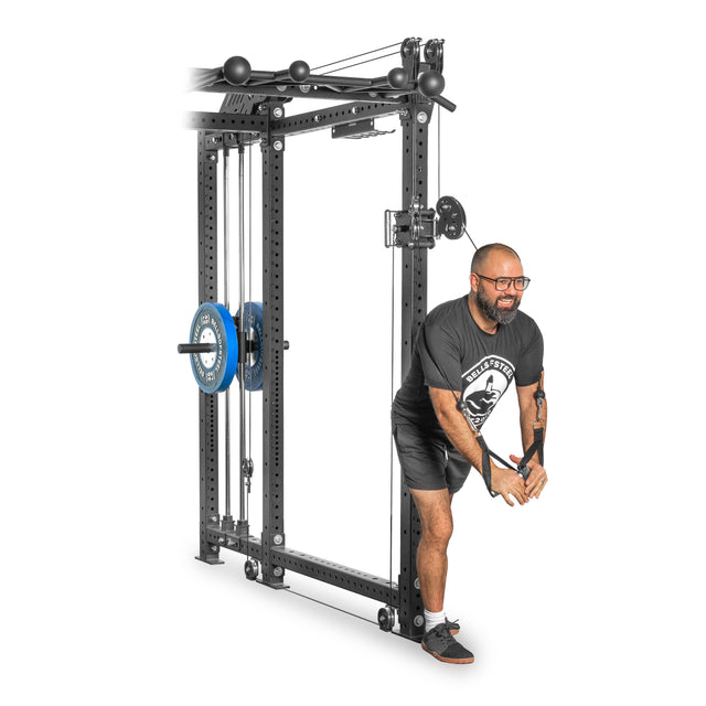 A person in shorts, a black t-shirt, and glasses exercises on a Bells of Steel Kraken Rack Attachment for 6 Post Manticore Racks. They skillfully pull the dual handles downward, adjusting the weights as needed.