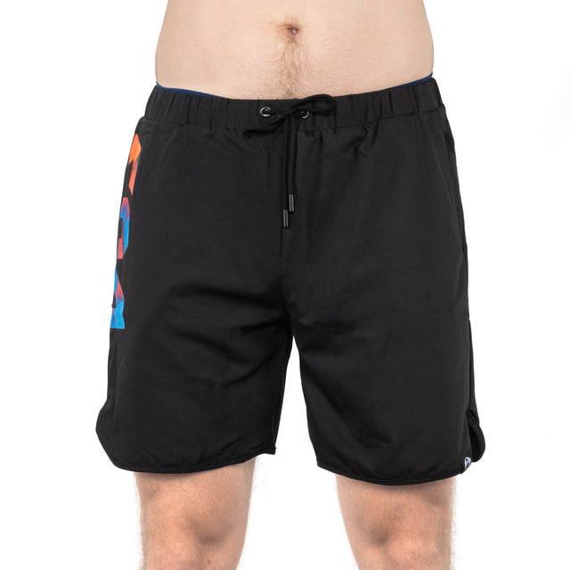 A person is wearing Bells of Steel Gym Shorts—black with a drawstring waist and colorful geometric design on the left side, made from stretchy fabric—shown from waist to above the knees against a white background.