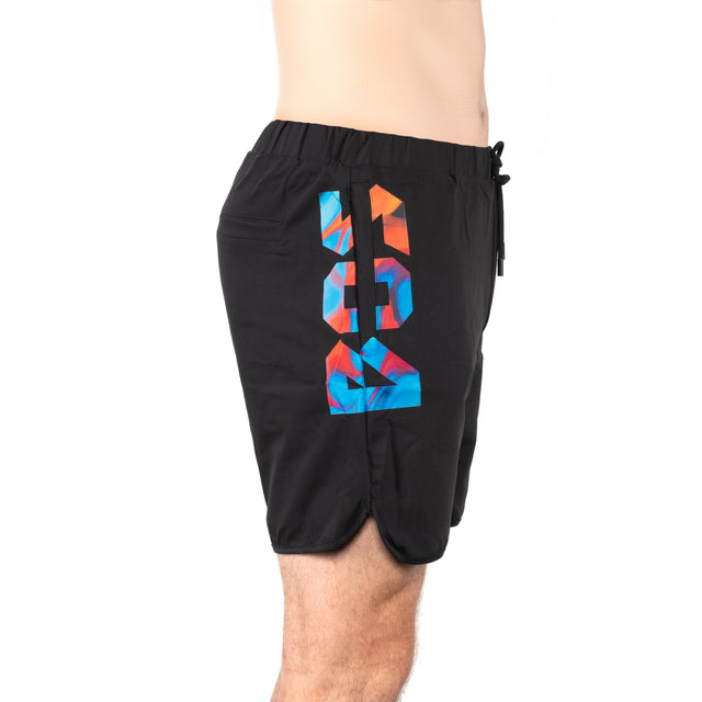 A person shown from the waist down wears Bells of Steel Gym Shorts in black, featuring a "16" in a colorful geometric pattern on the side, and is viewed from the side.
