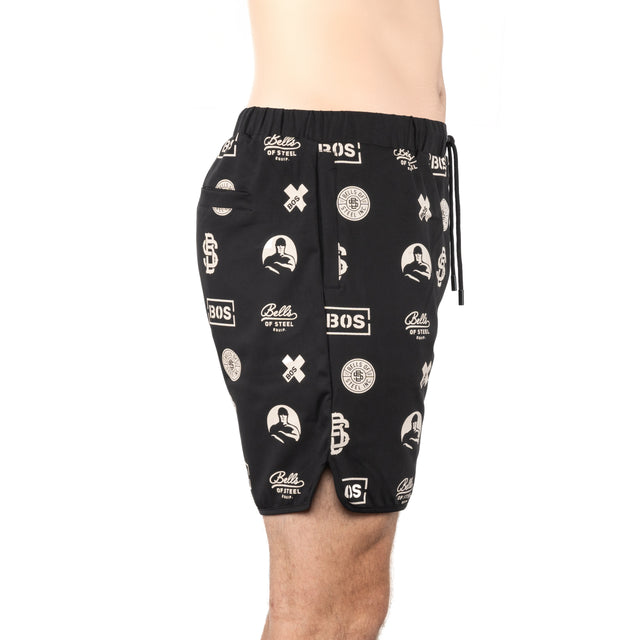 A person models Bells of Steel Gym Shorts—black, lightweight, stretchy fabric with white graphic logos and text—shown waist to just above the knee against a plain white background.