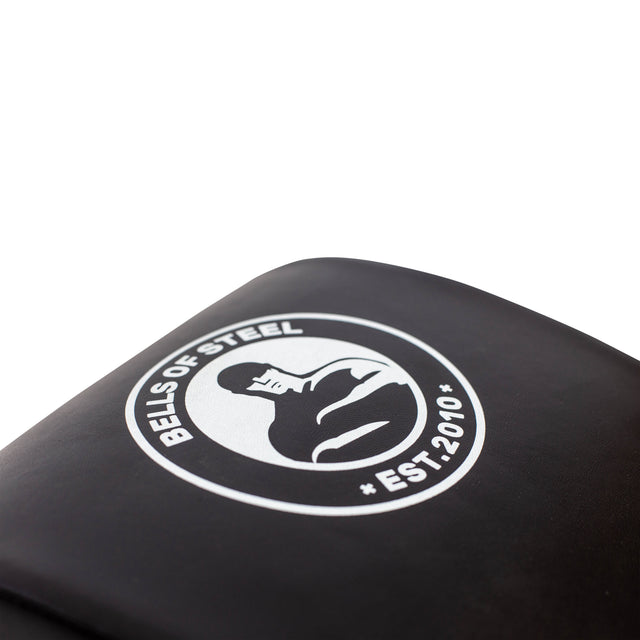 A close-up of a black Sit Up Mat displaying a white logo with a stylized person lifting weights, encircled by "Bells of Steel" and "EST. 2010". Ideal for core workouts, this symbolizes strength and dedication against a plain white background.