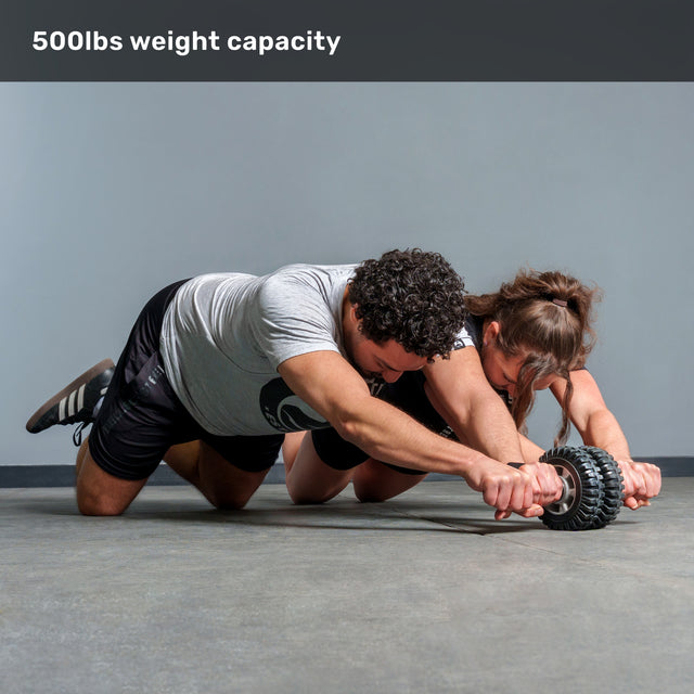 Two people kneel side by side, rolling the ABsyidyan Stainless Steel Ab Roller from Bells of Steel together. Text above them reads "500lbs weight capacity.