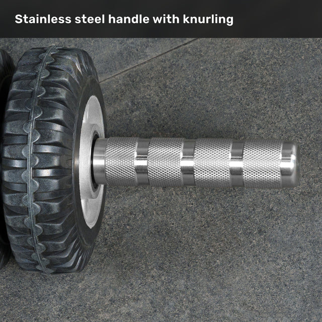 A close-up of the Bells of Steel ABsyidyan Stainless Steel Ab Roller with a knurled stainless steel handle, resting on a textured gray surface. The text above reads, "500 lb capacity stainless steel handle with knurling.