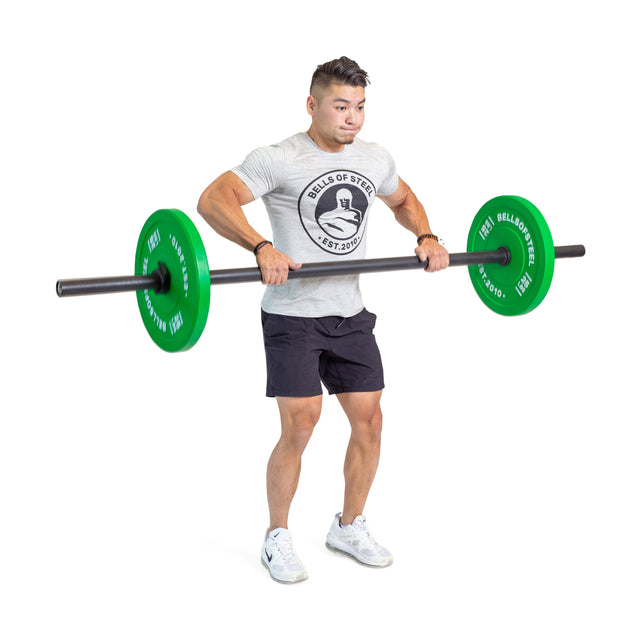 A man in a gray t-shirt and black shorts performs an upright row with Bells of Steel Axle Bars featuring green weight plates, lifting the bar to chest level against a white background and focusing on grip strength.