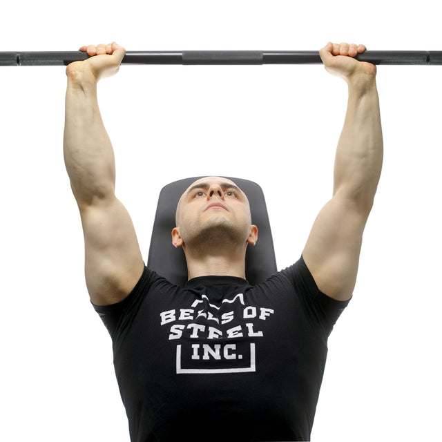 Wearing a black Bells of Steel T-shirt, a person presses the Bells of Steel Alex Leonidas Onyx Bar upward while lying on a bench, viewed from below.