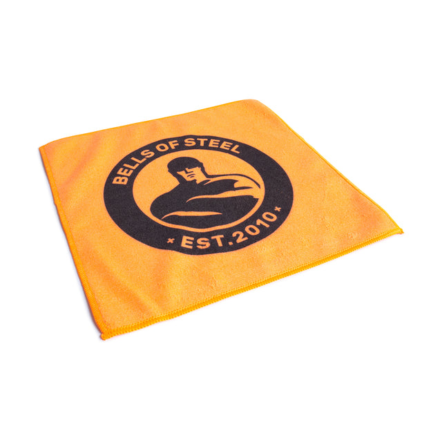 The Bells of Steel Barbell Cleaning Microfiber Cloth is an orange, lint-free towel with a black logo showing a muscular figure and "BELLS OF STEEL EST. 2010" in a circular design, displayed flat on a white background.