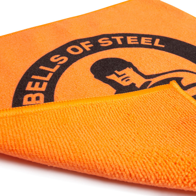 The Bells of Steel Barbell Cleaning Microfiber Cloth is an orange, lint-free towel featuring a black logo and a graphic of a muscular person, with a folded corner showing its texture and reverse side.
