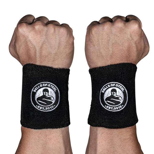 Two fists wear BellGuard Kettlebell Wrist Guards by Bells of Steel, featuring a white kettlebell and biceps logo on black fabric—ideal wrist and forearm protection for kettlebell lifters against a clean white background.