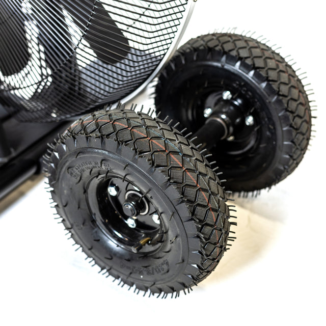 Close-up of two rugged black rubber tires with deep treads, mounted on a metal axle—part of the Bells of Steel Blitz Max Air Bike. A protective metal grill is visible against a white background.