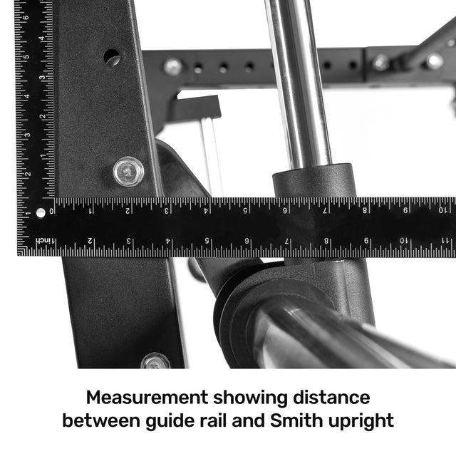 A close-up shows a black measuring ruler between the guide rail and Bells of Steel Smith Machine Rack Attachment on a power rack, demonstrating precise alignment and measurement.