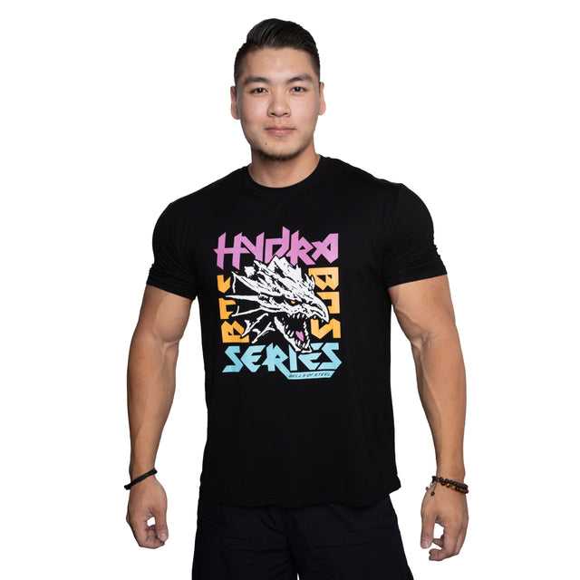 A man smiles, wearing the Bells of Steel Bamboo T-Shirt in black, featuring moisture-wicking fabric and colorful "HYDRA BEAST SERIES" text with a dragon head graphic. The background is plain white.