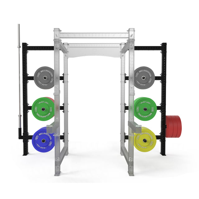 The Bells of Steel Hydra Batwing Storage, featuring 3x3 uprights, neatly organizes gray, green, blue, and yellow weights on both sides. A barbell is racked on the left, with multiple red plates stacked on the right.