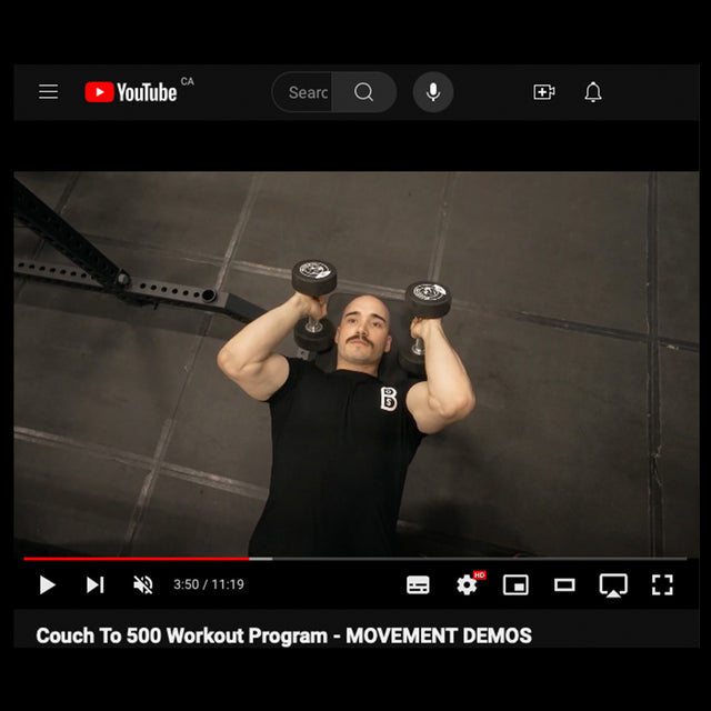 A person performs a bench press on a gym mat, holding dumbbells above their chest in the YouTube video "Couch to 500kg - Workout Program" by Bells of Steel, paused at 3:50/11:19, showing the transition from squats to upper body exercises.