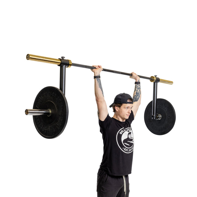 A person wearing a black cap and t-shirt lifts a Bells of Steel Camber Bar Attachment - Pair with two large, black weight plates featuring gold accents overhead against a white background.