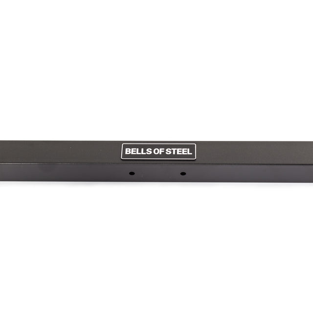 A close-up of a black metal bar from the Bells of Steel Cable Crossover (2.3" x 2.3" Racks), featuring a white "BELLS OF STEEL" label centered on the bar, with two small holes beneath the label.
