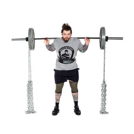 A tattooed man lifts a barbell with Bells of Steel Weightlifting Chains and weight plates, standing upright and facing forward, demonstrating progressive resistance against a white background.