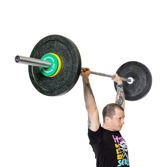 A man with tattooed arms lifts a loaded barbell with Bells of Steel Urethane-Coated Change Plates overhead while standing, wearing a black graphic t-shirt against a completely white background.