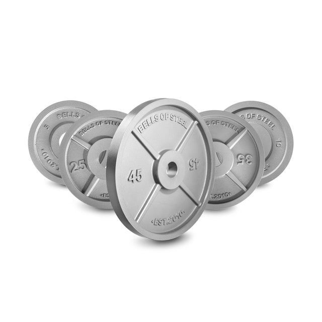 Five Bells of Steel Machined Iron Olympic Weight Plates—10, 25, 35, 45, and 100 lbs—are arranged in a row with the largest (45 lb) plate in front; each plate features precision holes for guaranteed fit and tolerance.