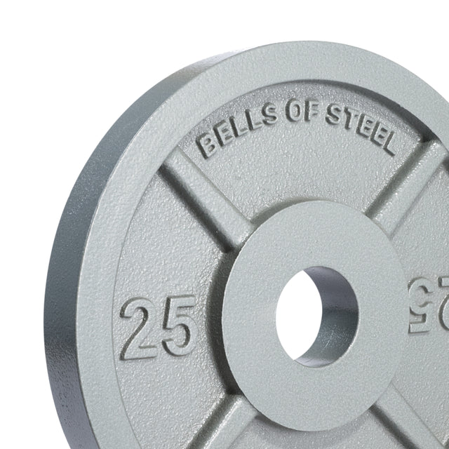 A close-up of a gray 25 lb Machined Iron Olympic Weight Plate by Bells of Steel, featuring a precision center hole and circular cutout for gym equipment. "BELLS OF STEEL" is embossed on the plate's surface.