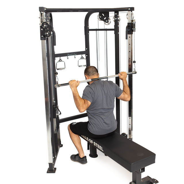 A man in a gray shirt, black shorts, and black sneakers is performing a lat pulldown on a cable machine using the Double Hook Straight Bar Cable Attachment by Bells of Steel.