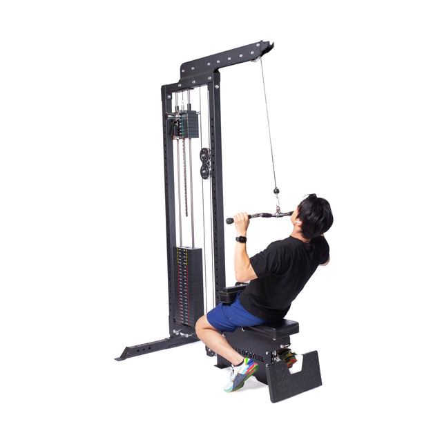 A person in a black shirt and blue shorts uses the Bells of Steel Multi Grip Curl Bar Cable Attachment on a lat pulldown machine, pulling it toward their chest for arm isolation, set against a plain white background.