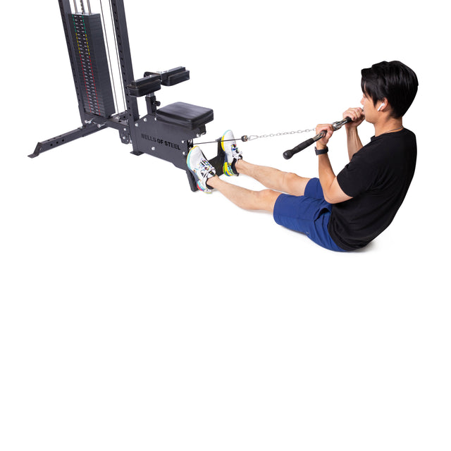 A person in a black shirt and blue shorts uses the Bells of Steel Multi Grip Curl Bar Cable Attachment on a cable row machine, pulling it toward their torso to isolate arm muscles.
