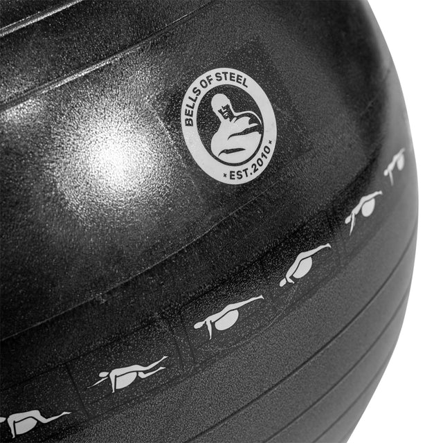 Close-up of a black Bells of Steel Exercise Ball with the logo, a kettlebell illustration, and "Est. 2010." Icons show a person in various workout poses, showcasing the ball's versatility.