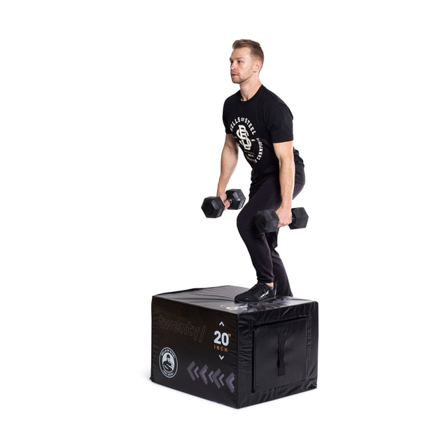 A man in black workout gear steps up onto the Bells of Steel 6-In-1 Soft Foam Plyo Box / Squat Box while holding dumbbells, highlighting this space-efficient and safe exercise equipment.