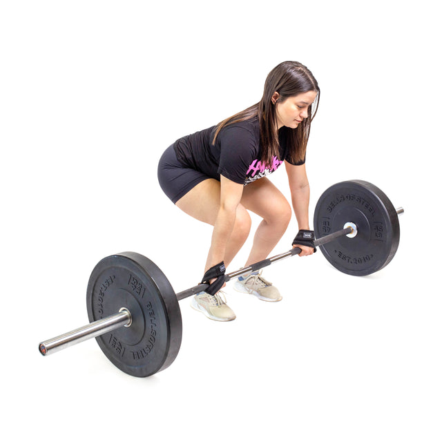 A woman wearing a black T-shirt, shorts, and gloves demonstrates her grip strength with Bells of Steel Classic Figure 8 Lifting Straps while gripping a barbell in the deadlift position against a white background.