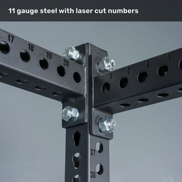 Close-up of the Manticore Flat Foot Power Rack Builder by Bells of Steel, featuring a black 11-gauge steel frame with visible bolts and precision laser-cut, numbered 1-inch holes. Text at top reads, "11 gauge steel with laser cut numbers." This heavy-duty 3"x3" power rack is perfect for building a robust home gym setup.