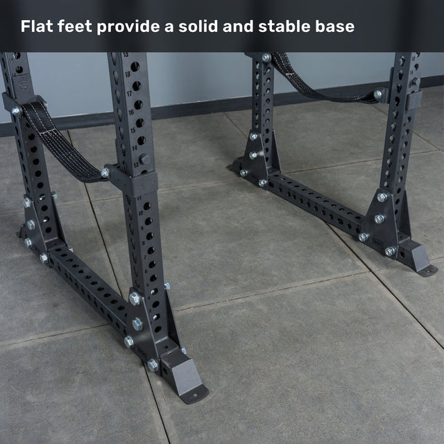 Close-up of the flat base feet of the Bells of Steel Manticore Flat Foot Power Rack - Prebuilt (3" x 3", 1" Holes) on a tiled floor, with text above reading, "Flat feet provide a solid and stable base." Perfect for any home gym setup.