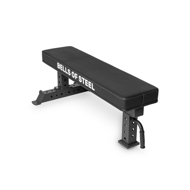 The Bells of Steel Powerlifting Flat Bench, with a durable vinyl surface and adjustable feet, features sturdy metal legs for stability. It has a 000lb max capacity with "Bells of Steel" etched on the side, making it ideal for powerlifting in any workout environment.