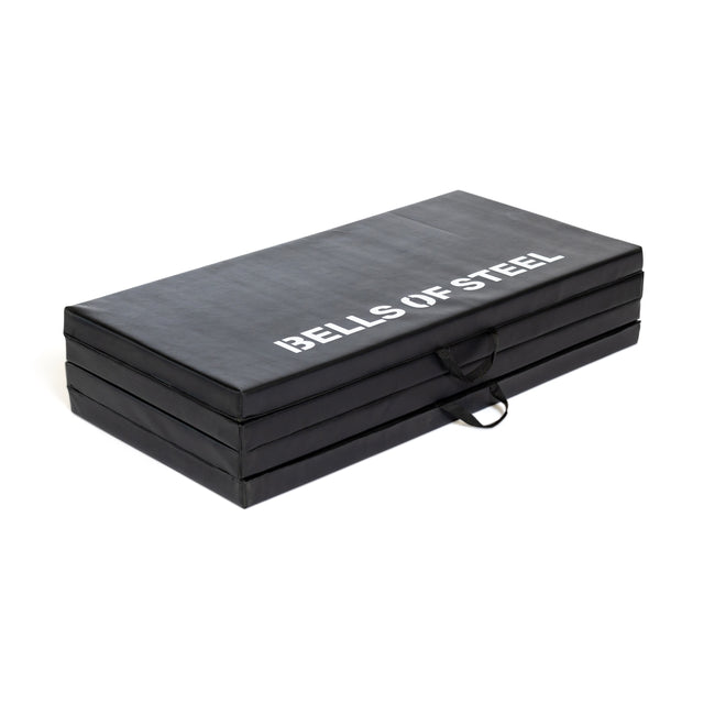The Bells of Steel Four Fold Mat is a black gym mat with a carrying handle and "BELLS OF STEEL" in white on top, designed for easy transport and versatile workouts.