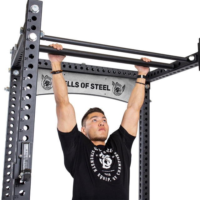 A person in a black T-shirt does a pull-up on the Bells of Steel Fat/Skinny Pull Up Bar, which is attached to a power rack.