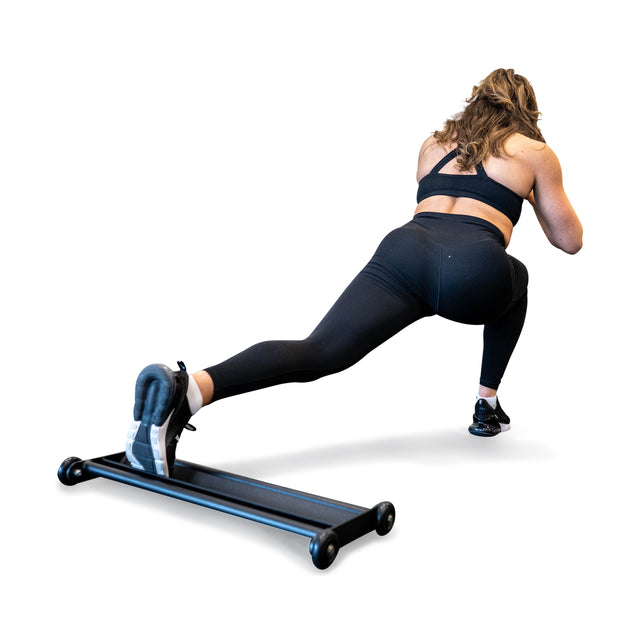 In black workout attire, a woman performs a low lunge with her left foot on the Bells of Steel Glute Ham Slider, designed for hamstring blasting. Her pose is highlighted against a plain white background, showcasing this innovative, space-efficient equipment.