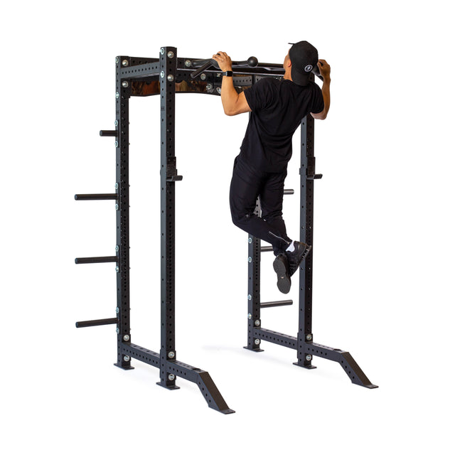 Wearing black athletic clothing and a cap, a person performs a pull-up using the Bells of Steel Globe Pull Up Bar, featuring a sturdy steel frame with multiple weight plate holders, enhancing grip strength against a white background.