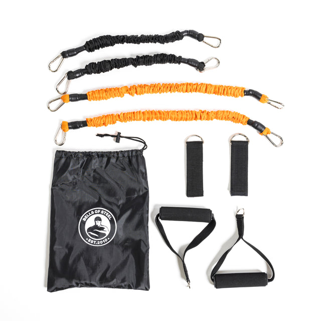 The Bells of Steel Soft Glute Bench, shown on a white background, is ideal for glute bridges and strength training. The set includes two black and two orange bands with carabiner clips, handles, ankle straps, and a drawstring bag.