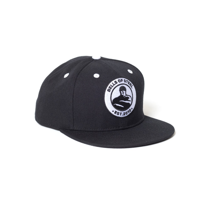 The Bells of Steel Snap Back Hat is a black classic snapback with a round white front patch showing "BELLS OF STEEL EST. 2010" and a kettlebell lifter illustration.