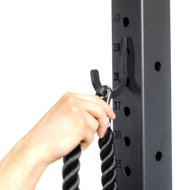 A hand secures a thick black rope to the Bells of Steel Utility Hook on a metal rack with numbered height markings, creating an ideal gym storage solution.