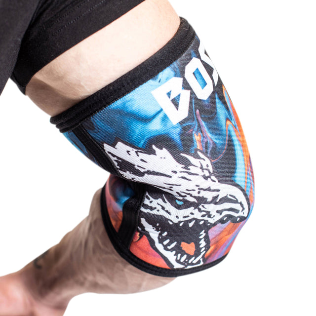 A close-up of a bent arm wearing Bells of Steel Elbow Sleeves, featuring a fierce white wolf graphic and bold white letters on a black and blue background.